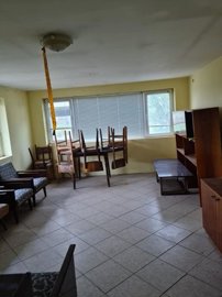 Interior room with tiled floor, several chairs stacked on a table, and wooden shelves along the walls.
