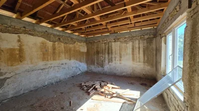 Room showing exposed wooden roof structure, unfinished walls, and two white-framed windows with one window pane detached.