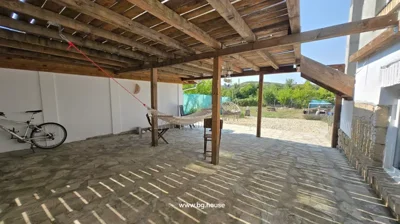 Covered outdoor patio with stone floor, wooden beams, hammock, hanging chair, and bicycle